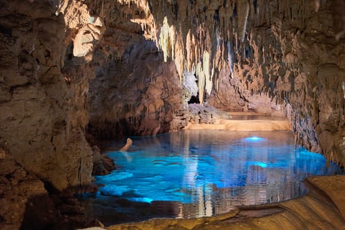 Image of light shining into a blue pool of waterbeneath stalagtites