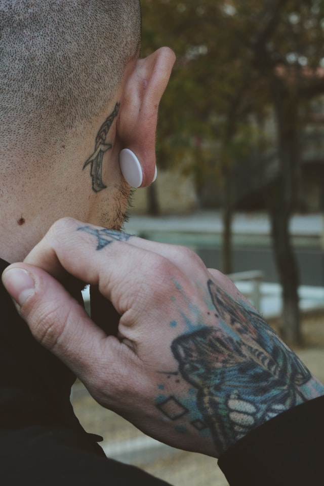 Back of shaved head; white gauge in ear; dagger tattoo behind ear
