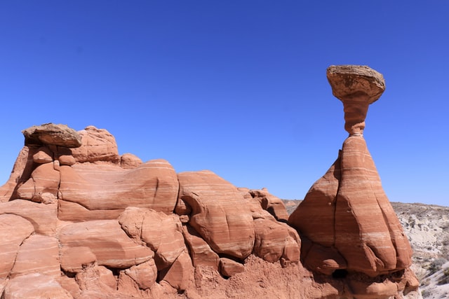 A formation of tall, red rocks, including a screw-shaped rock balancing precariously on top of a rock shaped like an upside down top.